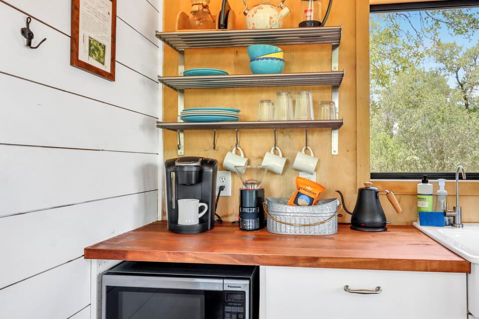 Your cozy kitchen corner has everything you need: a coffee station, open shelves stocked with dishes, and peaceful tree views through the window—perfect for your morning ritual.