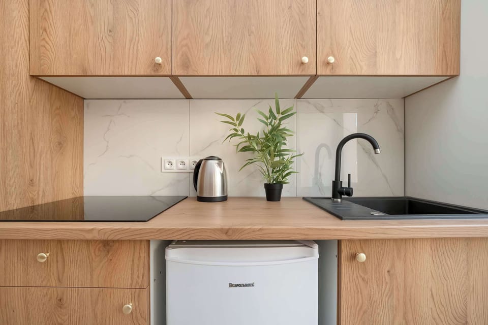 A modern kitchenette with light wooden cabinetry, a small sink, and a minimalist design. Perfect for compact, functional use in a studio.