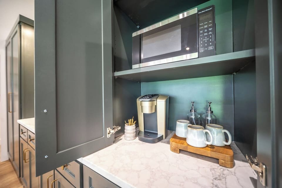Built-in coffee station with microwave and single-serve coffee maker, stocked with coffee, flavored syrups, creamer, sweeteners, and coffee bar essentials for an easy, elevated morning routine.