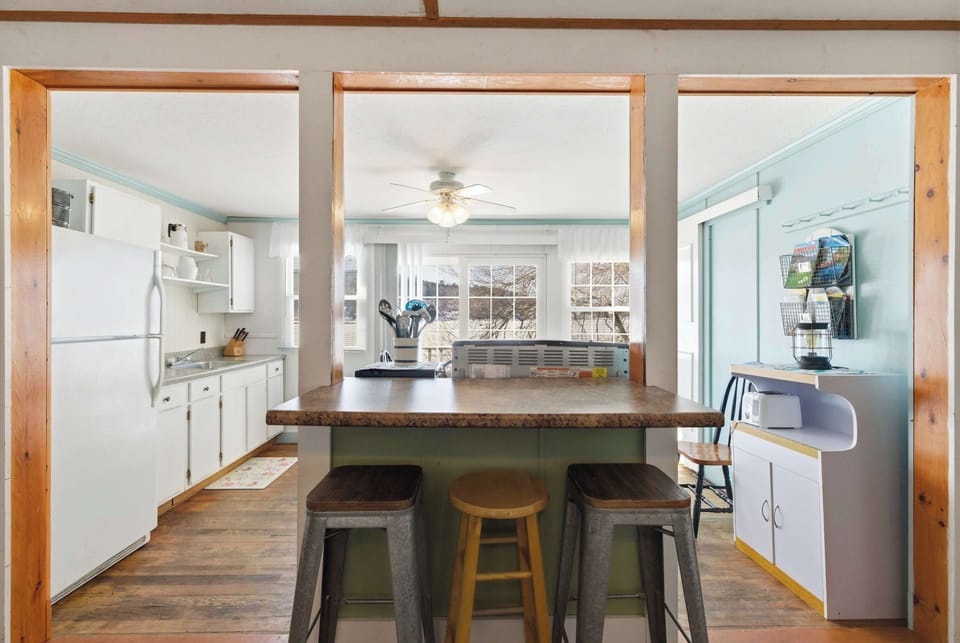 The open kitchen and breakfast bar, with stools pulled up and the lake visible through the windows beyond — casual mornings start here.