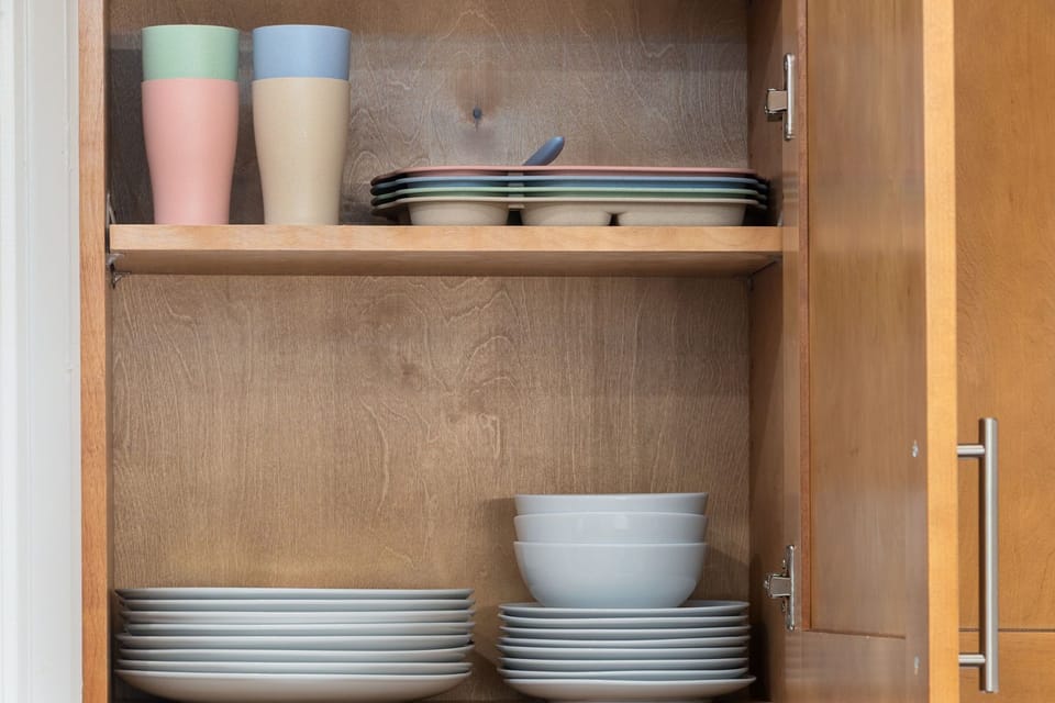 Well-stocked kitchen cabinet with organized dishes, bowls, and colorful cups