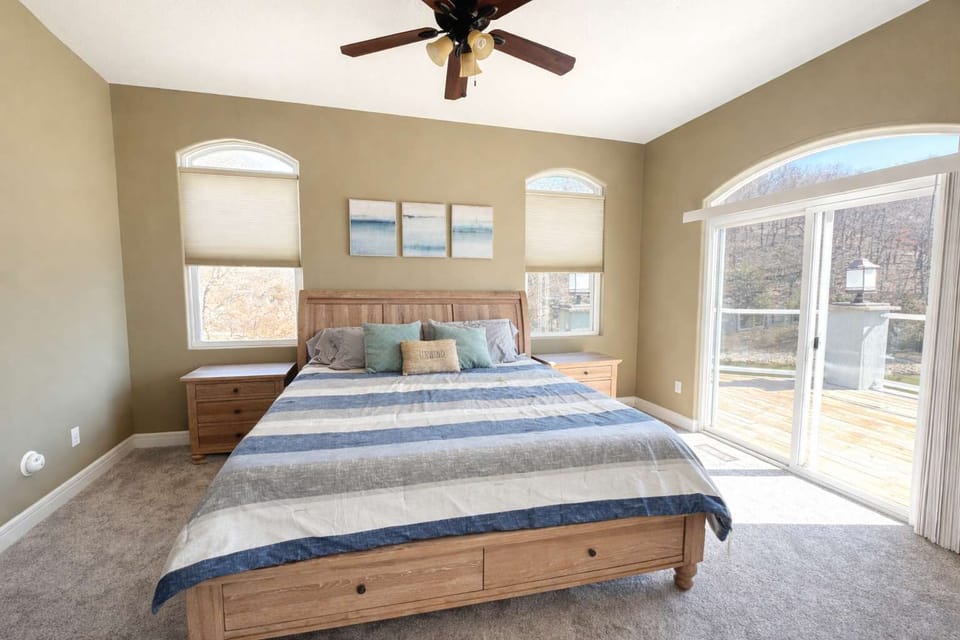 Relax in this bright bedroom featuring comfortable bedding, arched windows, and easy access to beautiful outdoor scenery.