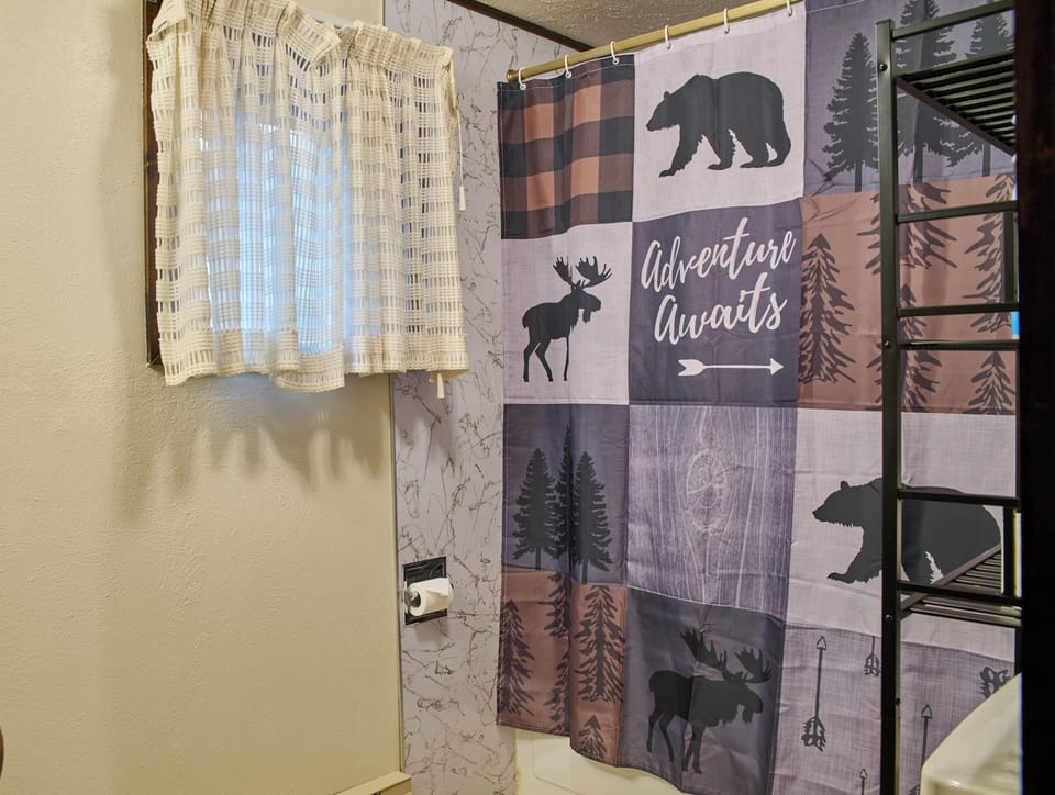 Bathroom view focused on the tub-and-shower combination with a woodland-pattern curtain.