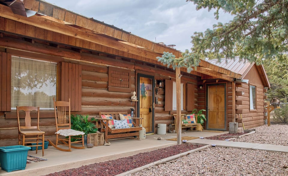Close exterior view of the log cabin's covered front porch with two entry doors and assorted wooden seating.