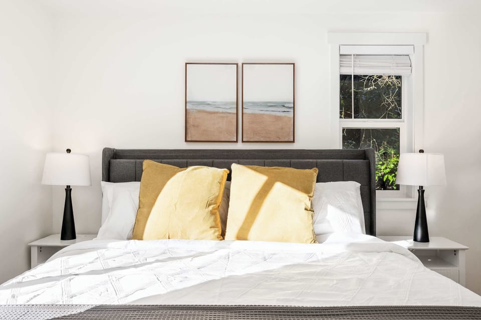 Experience the perfect blend of comfort and style in this cozy bedroom. The warm yellow pillows add a cheerful touch, while minimalist coastal artwork above the bed creates a soothing, beachy vibe.
