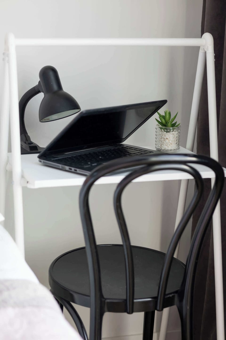 A small workspace with a black chair and desk lamp, perfect for remote work or study. Conveniently placed near a bedroom.