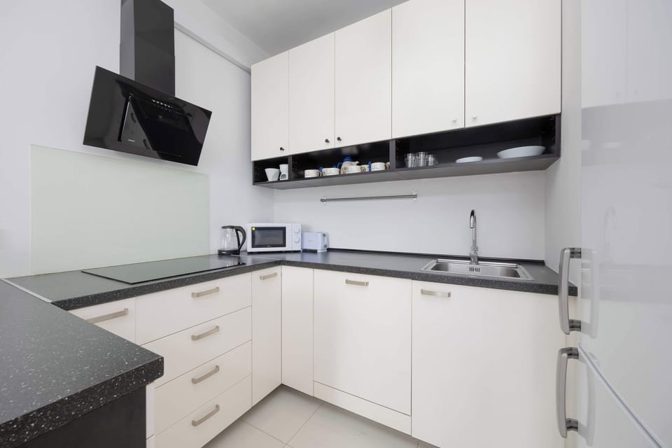 A modern, fully equipped kitchen with white cabinetry and black countertops. Includes an oven, gas stove, and hood.