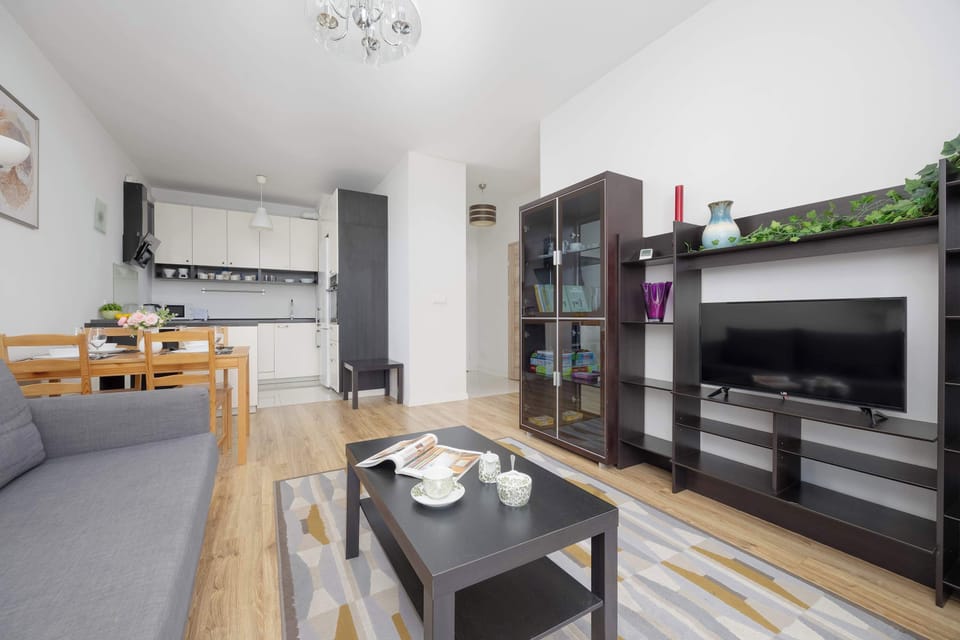 A bright, spacious living room with a grey sofa and natural light streaming through sheer curtains. Stylish decor and a rug bring warmth to the room.