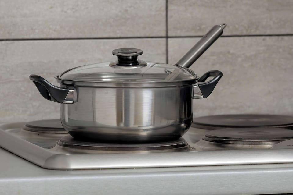 A close-up shot focuses on a stainless steel pot with a lid sitting on the stovetop. Grey wall tiles provide a practical and aesthetic finish to the cooking area.