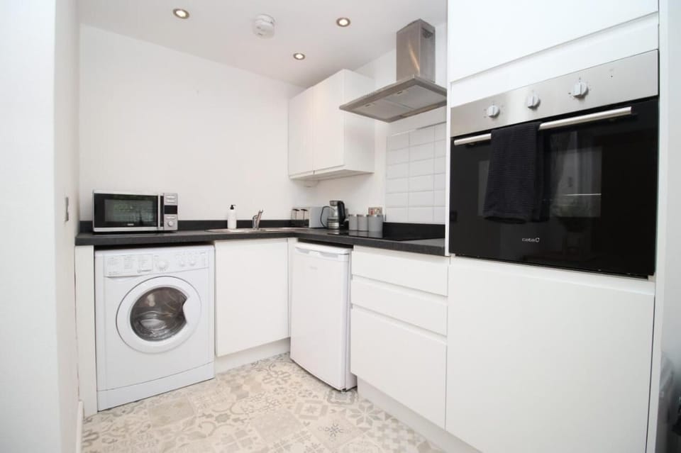 This kitchen features crisp white cabinets, black counters, and integrated appliances including ovens, microwave, and washer. Light patterned flooring complements the modern furniture for a clean, inviting look.