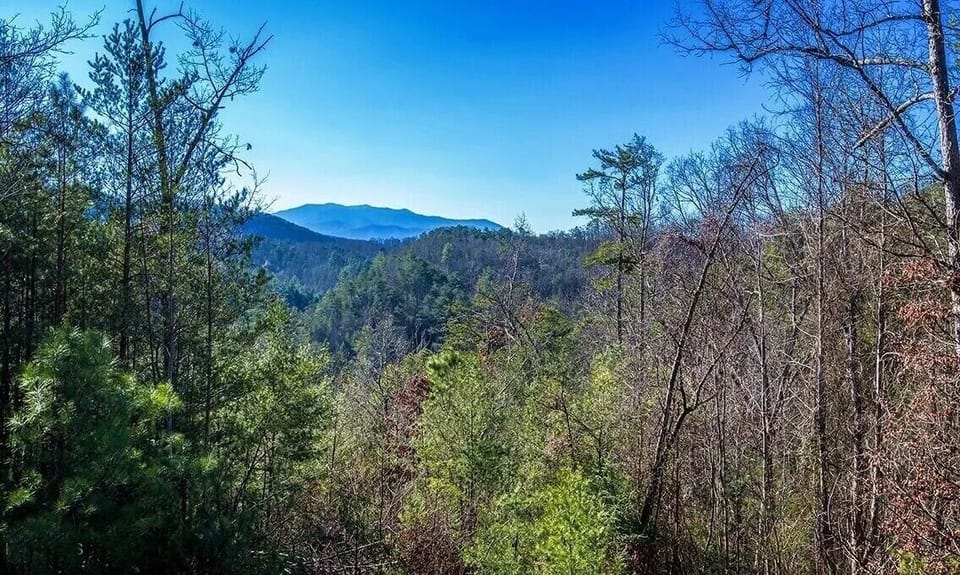 Rolling mountain vistas stretch endlessly beyond forested hills, offering a peaceful retreat surrounded by natural beauty.