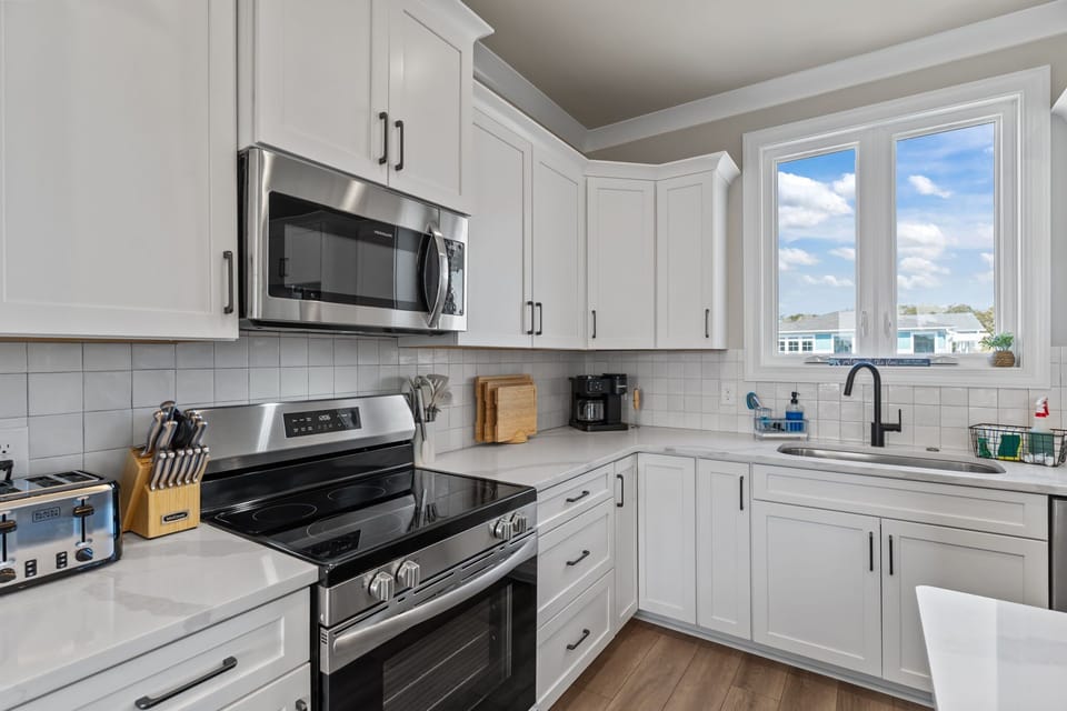 Bright Coastal Kitchen w/ Stainless Steel Refrigerator, Built-In Microwave, Electric Range Oven, Dishwasher, Large Island Seating, Pendant Lighting, and Natural Light