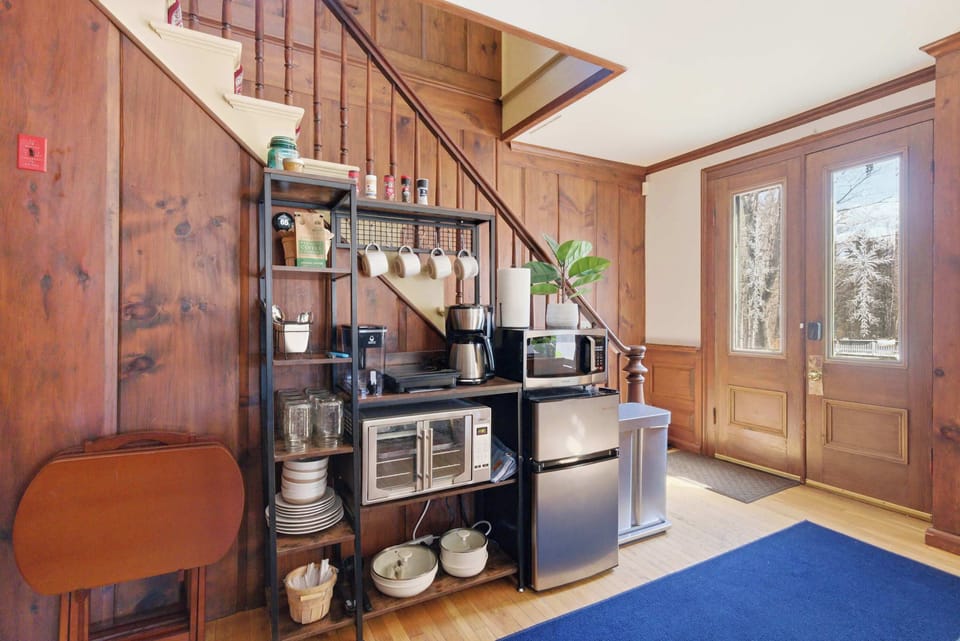 The kitchenette tucked under the staircase, with the convection/air fryer oven, microwave, mini fridge, and private entrance door just beyond.