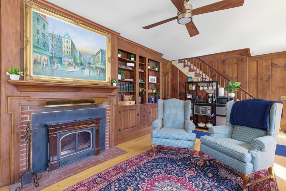 The fireplace and built-in bookshelves anchor the living room, with the oil painting above the mantel and the staircase leading up behind.