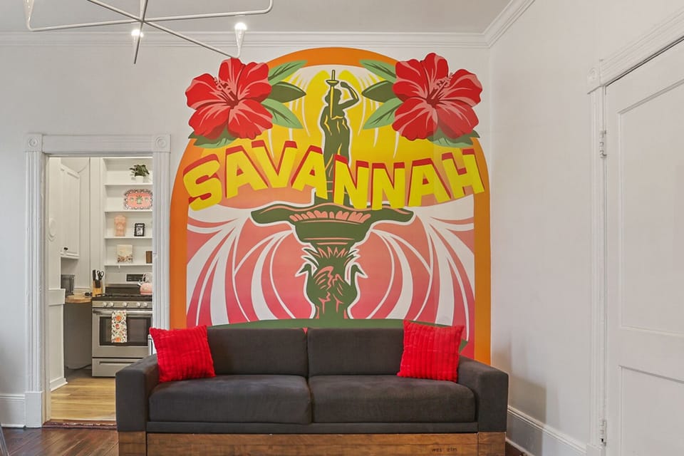 The downstairs living room features cozy seating and a beautiful Savannah-inspired mural that adds local character.