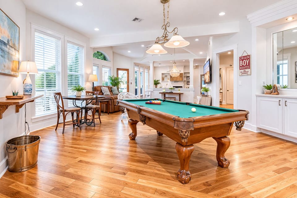 Game room with pool table, open dining area, and hardwood floors – perfect entertainment space for large groups in Galveston vacation home.