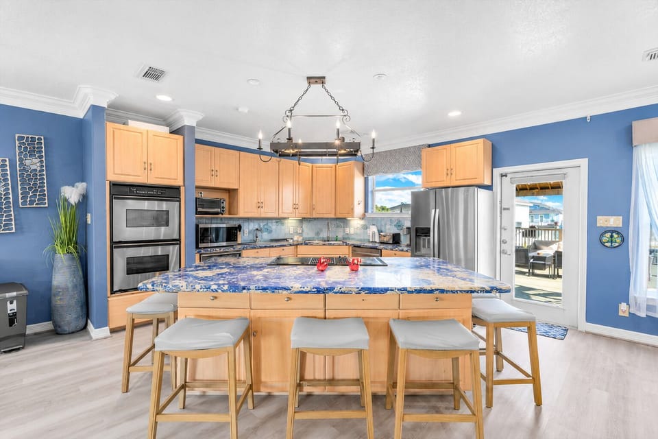 Bright Galveston vacation rental kitchen featuring a spacious granite island with seating for four, stainless steel appliances and ample space for group meal preparation.