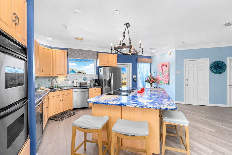 Fully equipped kitchen with a large blue granite island, breakfast seating, stainless steel refrigerator, dishwasher, double wall ovens and generous cabinet storage.