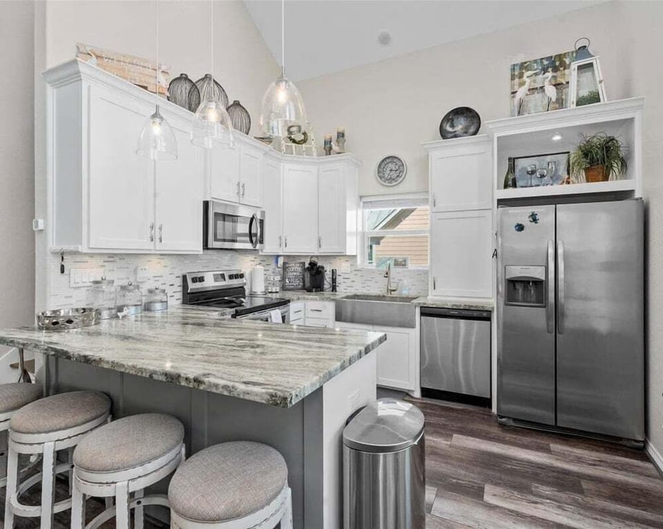 Fully equipped coastal kitchen with granite countertops, stainless steel appliances, and bar seating for guests.