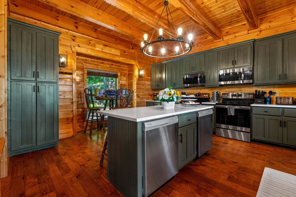 Spacious living room with leather sofas, fireplace, antler chandelier, mountain-view windows, and open access to kitchen and dining.