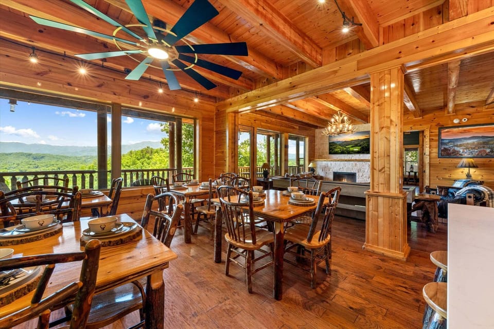 Spacious dining area with multiple wood tables, warm wood finishes, ceiling fan, and scenic mountain views through expansive windows.