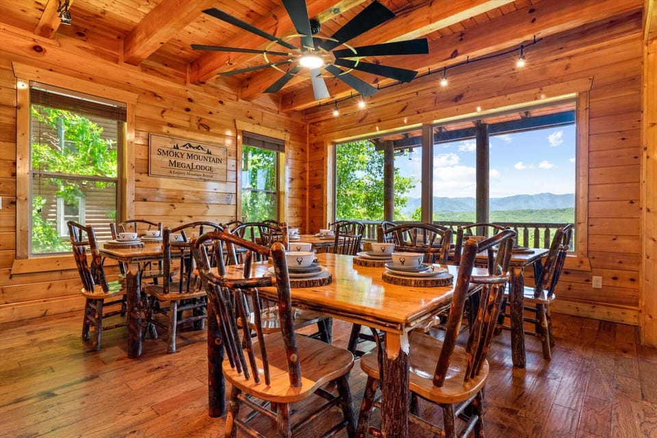 Rustic bar-height dining table with log chairs, wood floors, cabin walls, and nearby lounge chair in an open lodge layout.