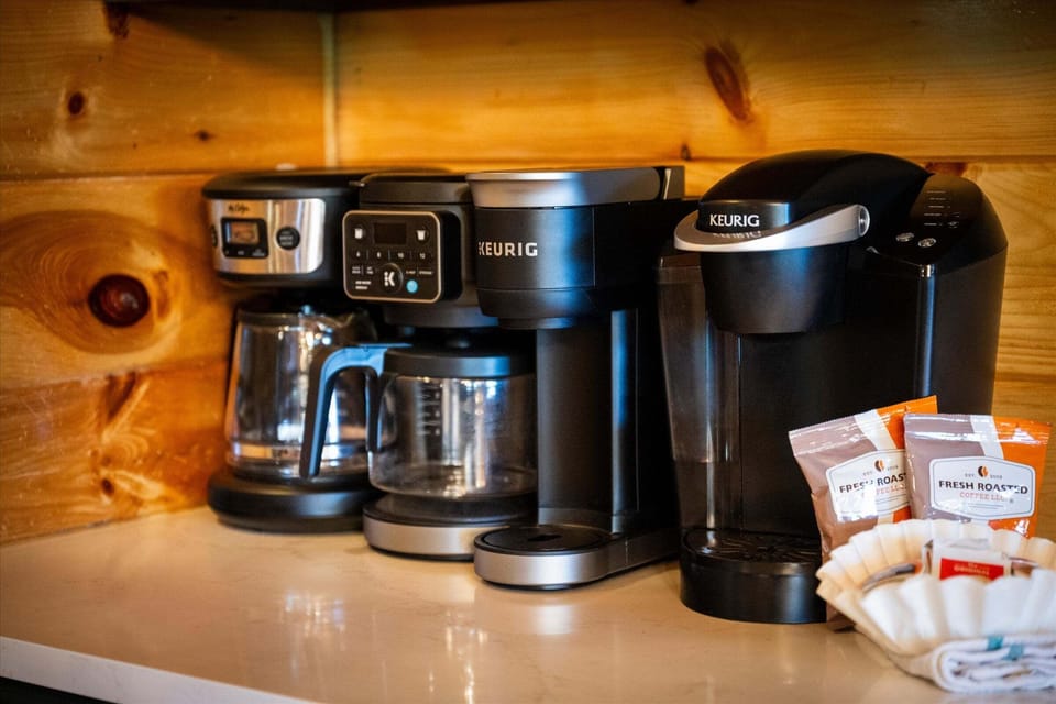 Kitchen coffee station with Keurig machines, drip coffee makers, coffee filters, and coffee packets on a cabin countertop.