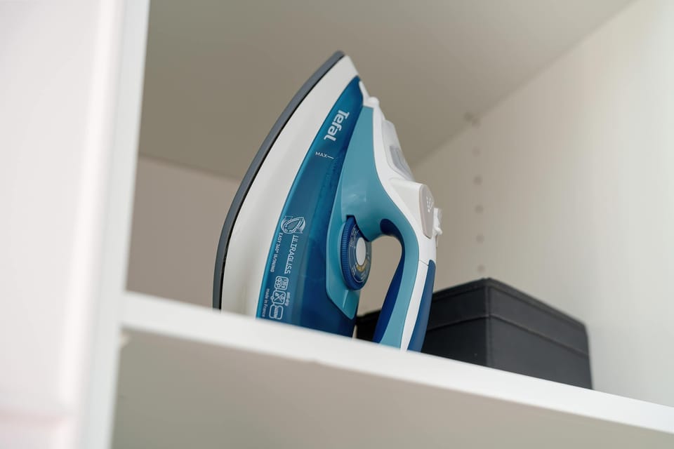 An open wardrobe shelf holds a modern blue steam iron, ensuring guests can keep their clothes crisp and neat. This practical amenity reflects the apartment's high standard of service.
