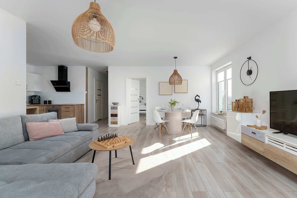 A panoramic view of the multifunctional living space shows the seamless transition between the kitchenette, dining, and relaxation areas. Bright wooden floors and white walls tie the entire interior together.