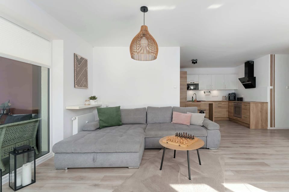 A stylish grey sofa is paired with a round wooden coffee table in a light-filled living room. The Scandinavian-inspired decor is complemented by a designer wicker pendant lamp.