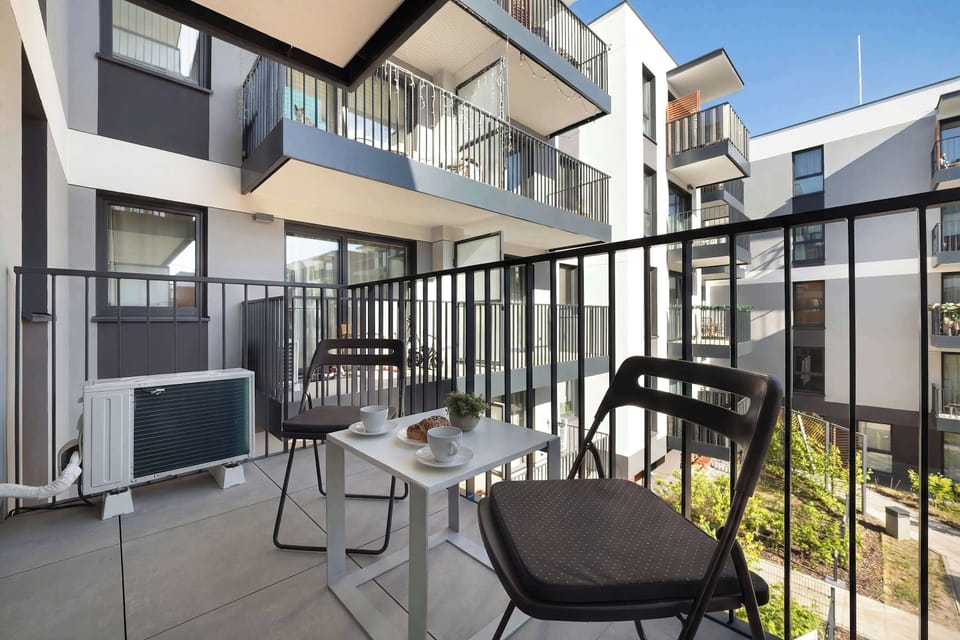A balcony is shown with a large table and two black chairs. It seems a lovely place for a couple to sit and have some snacks while enjoying the view.