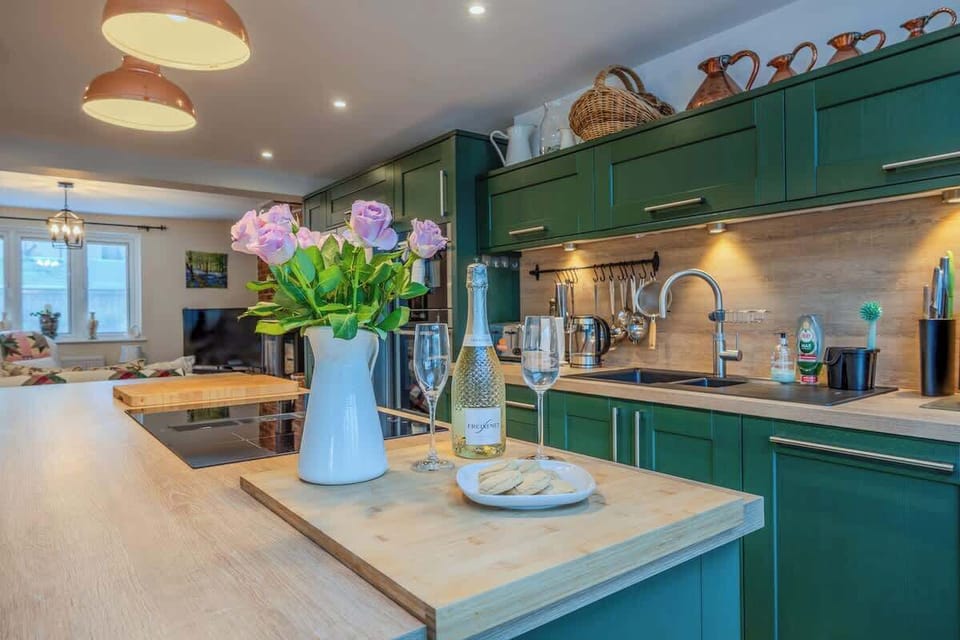 A welcoming open-plan kitchen and lounge with green cabinetry and plants adding a touch of nature, centered around a sociable island ideal for gathering and relaxing together.