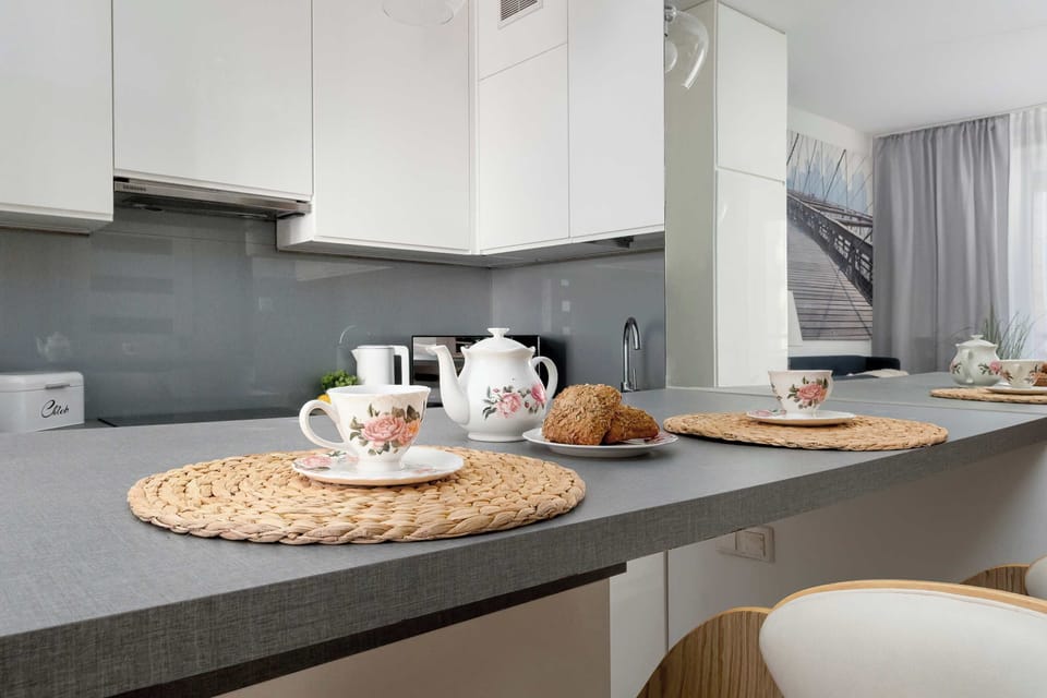 A close-up of the bar counter, displaying porcelain tableware and small snacks. The mirror on the wall adds depth and reflects fragments of the modern kitchen.
