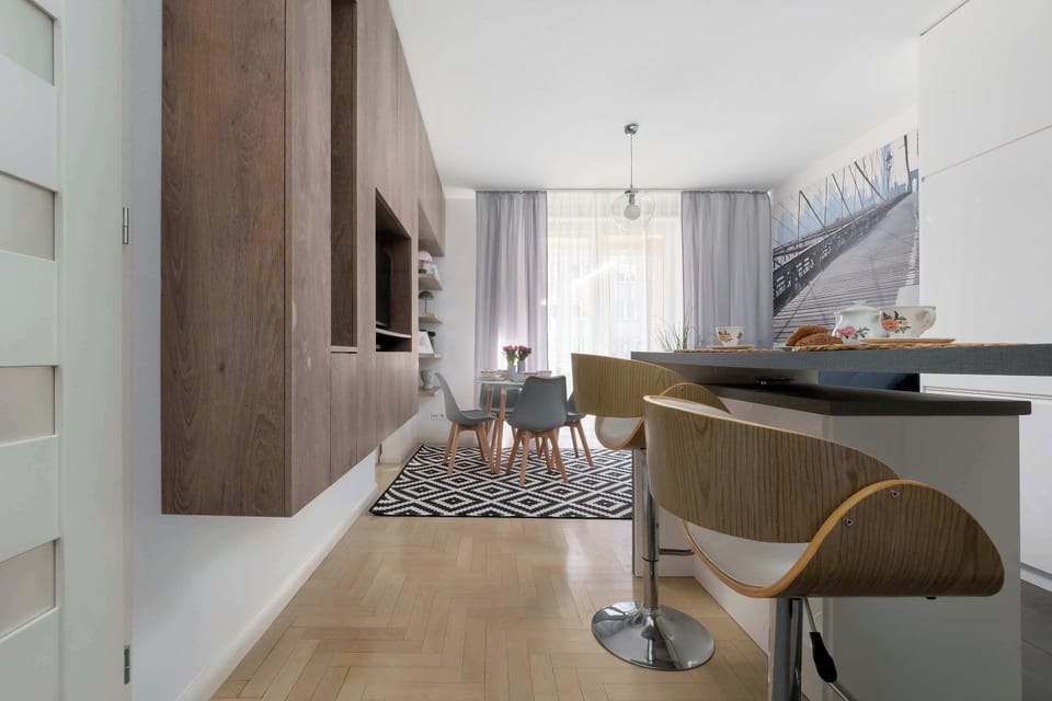 A long hallway leading to the living room, with warm wood-toned built-in furniture. On the right is a bar with high stools, perfect for a quick breakfast.