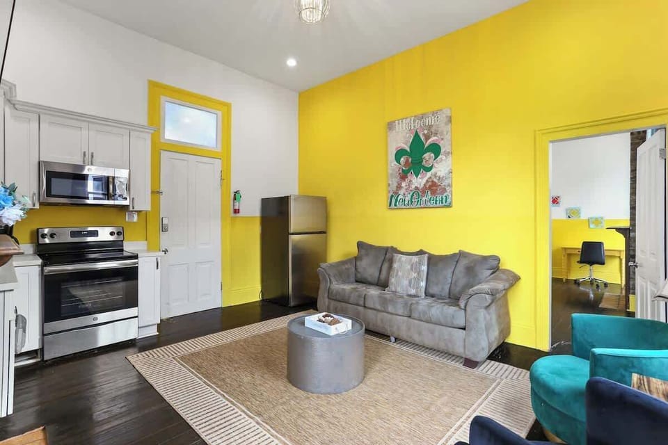 Open living area with comfortable seating, bold New Orleans–inspired décor, and a Smart TV. Bright, inviting layout that flows seamlessly into the kitchen—perfect for relaxing after a day in the city.