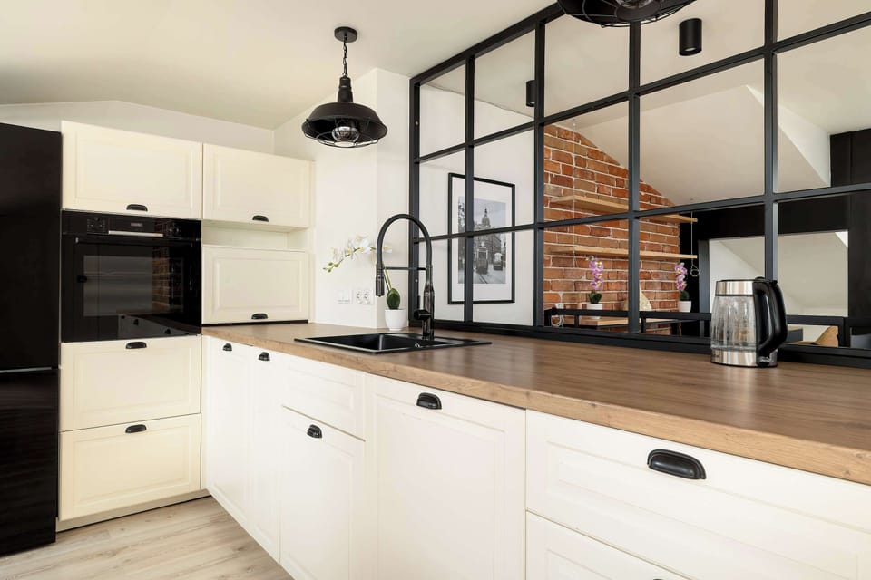 A modern kitchen workspace features a black glass backsplash and high-end built-in appliances. The large window partition allows light to flow between the kitchen and the living area.
