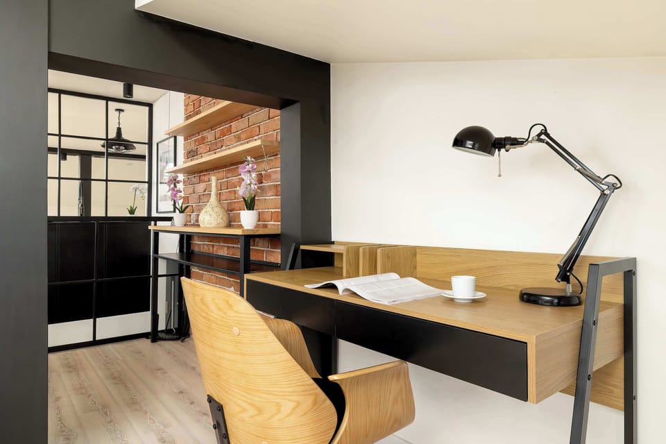 A dedicated workspace includes a sleek wooden desk and a modern chair tucked under the sloped ceiling. A black adjustable lamp provides focused lighting for tasks.