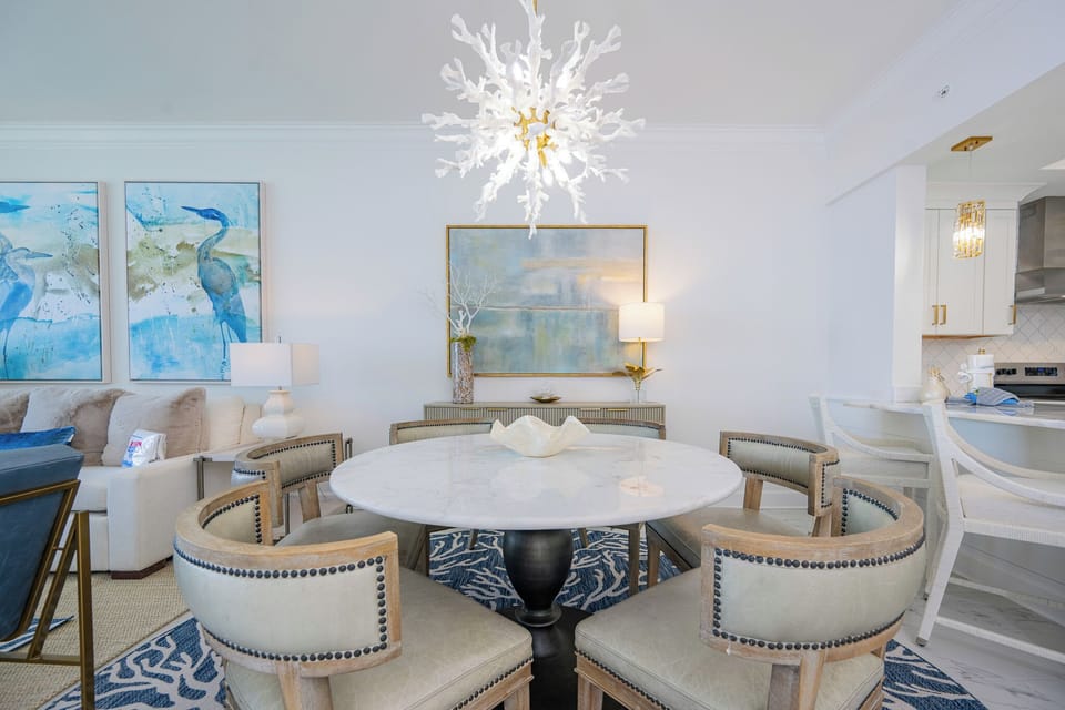 Round marbled table invites laughter and shared stories in the dining area beside coastal-inspired artwork and soft lighting