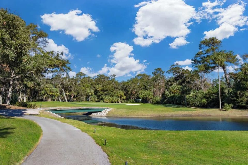 Scenic golf course with a water hazard and surrounding trees under a blue sky.