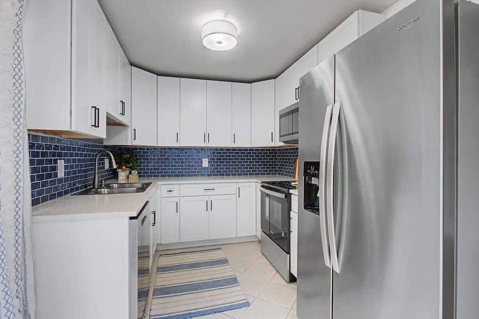 Your sleek, fully-equipped kitchen features pristine white cabinets, stylish blue subway tile backsplash, and premium stainless steel appliances for culinary adventures.
