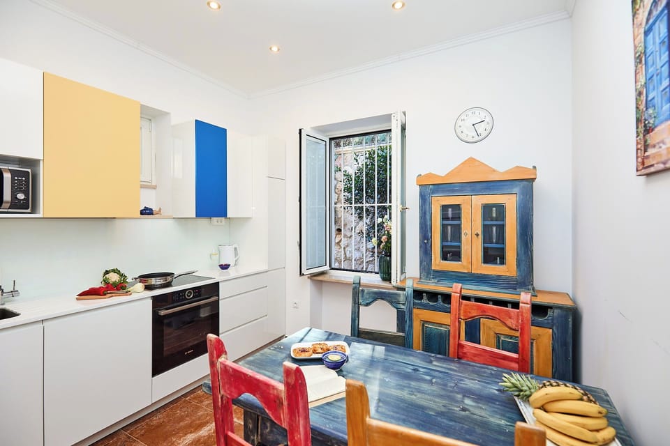 A charming blend of modern amenities and rustic character, the fully equipped kitchen features sleek white cabinetry alongside a vibrant, handcrafted dining set.
