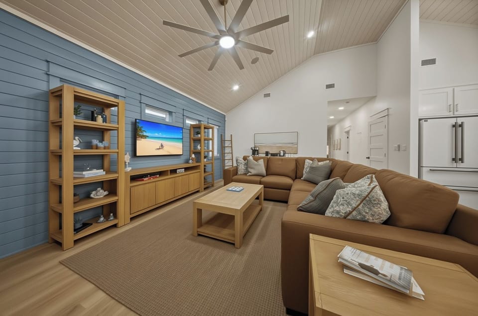 Bright, beachy living room goals—vaulted ceilings, oversized sectional, and a big-screen setup for movie nights after the sand.
