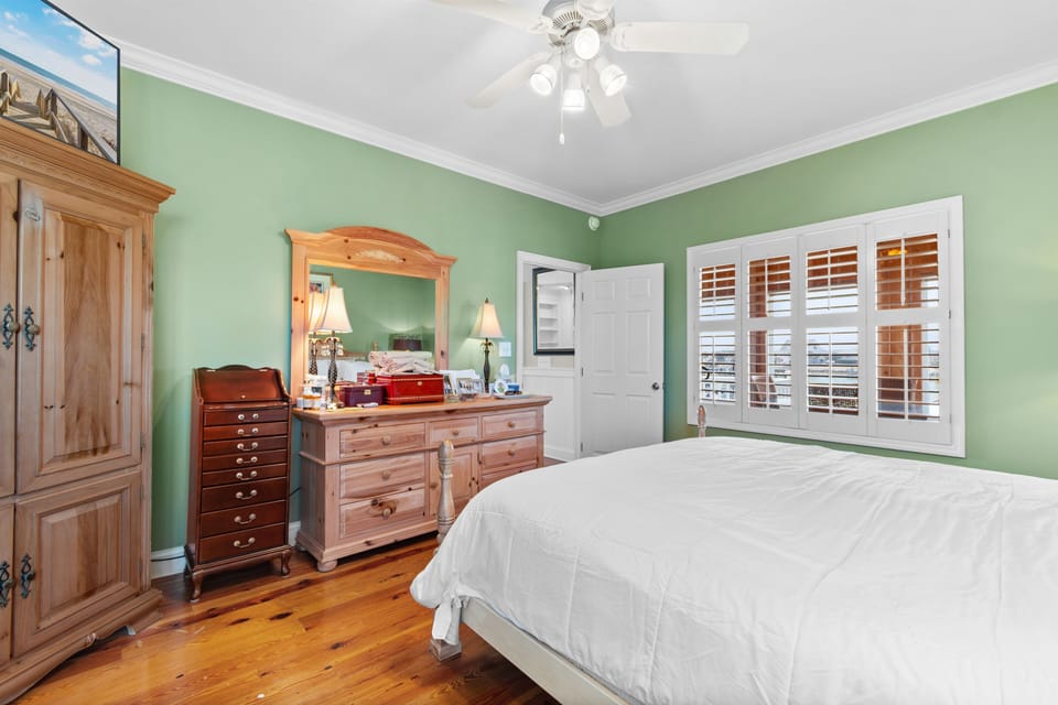 Rest peacefully in your charming bedroom with soothing green walls, warm wood floors, and natural light filtering through plantation shutters.