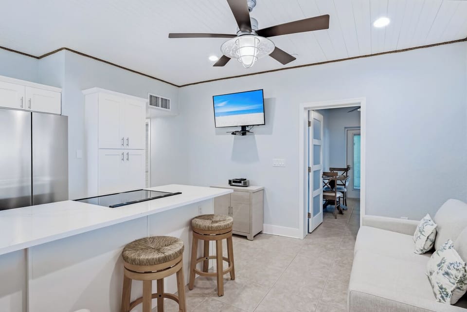 Your modern kitchen features sleek white countertops, stainless steel appliances, and comfy bar seating—perfect for cooking and casual dining together.