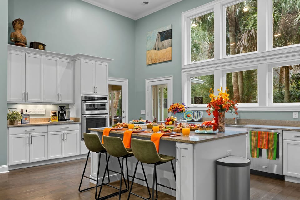 Bright, modern kitchen with soaring ceilings and oversized windows that flood the space with natural light—perfect for morning coffee or cooking together after a beach day.