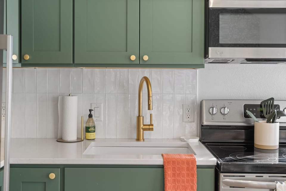 Kitchen sink with quartz counters, gold faucet, and tile backsplash.