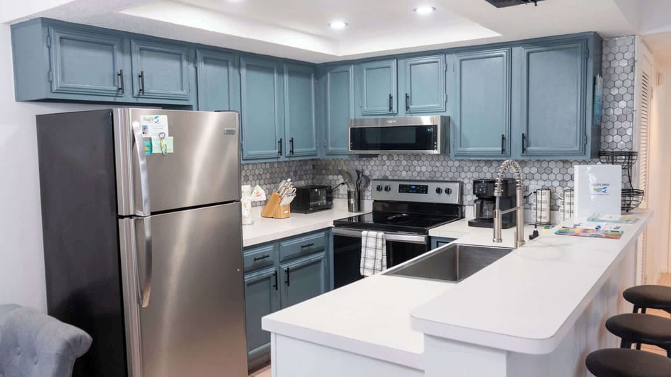 Modern kitchen with blue‑gray cabinetry, stainless appliances, and a bright island workspace. Patterned tile backsplash and thoughtful essentials create a clean, functional space perfect for cooking, gathering, and effortless vacation living.