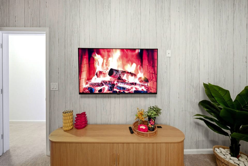 Relax in this welcoming living space, complete with a stunning wall-mounted TV and a cozy fire to create a warm atmosphere. Soft textures and natural accents, like a lush plant, make it an ideal retreat for all.