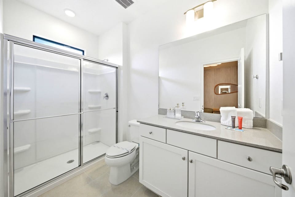 Enjoy a bright, clean bathroom featuring sleek white cabinetry and a spacious glass-enclosed shower. With modern fixtures and ample counter space, it guarantees comfort and a refreshing experience throughout your stay.
