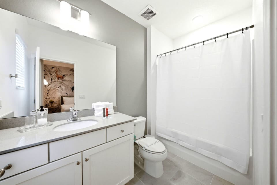 Experience a bright and airy bathroom with a spacious vanity and large mirror that amplify natural light. Neutral tones create a calming vibe, and the clean shower area ensures functionality for your stay.